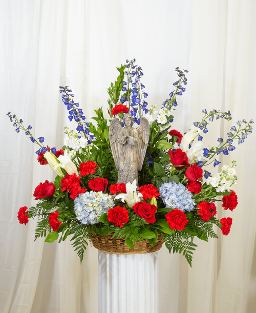 A one-sided Patriotic arrangement designed in a 14 inch basket with lilies, roses, hydrangea, delphinium, stock, carnations, and statice. Suitable for a funeral or memorial service with14.75 inch keepsake praying angel. Overall 32 inchH x 31 inchW