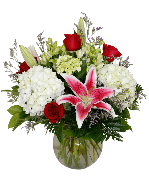 A 7-3/4 inch glass vase holds an all around arrangement with four red roses, hydrangea, mini green hydrangea, lilies, charmelia alstroemeria, and caspia. 18 inchH x 19 inchW