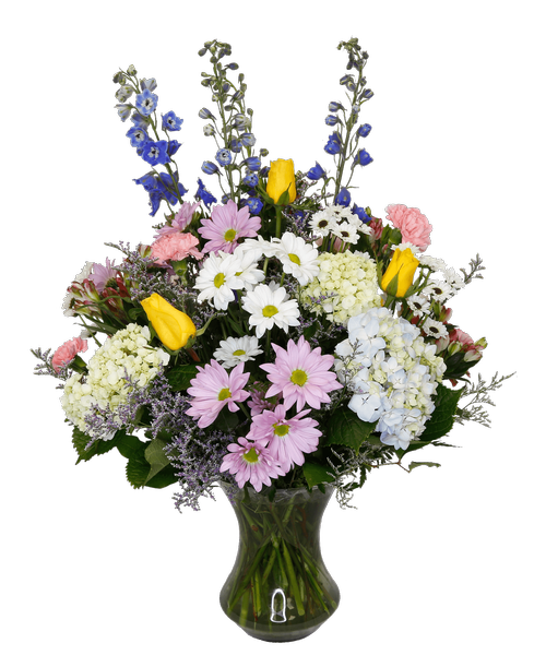 A 9.5 inch glass vase holds an all-around arrangement with four yellow roses, blue hydrangea, mini green hydrangea, pink charmelia alstroemeria, blue delphinium, pink carnations, white and lavender daisy poms, yin yang poms, and caspia. Overall 31 inchH x 22 inchW