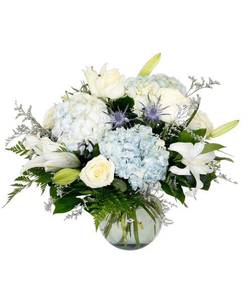 A 7-3/4 inch glass vase holds an all around arrangement in white and blue including six roses, four hydrangea, lilies, eryngium, and caspia. 17 inchH x 15 inchW