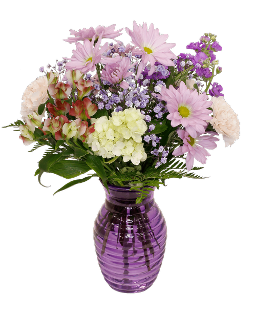 A 7.25 inchH purple glass vase with a horizontal design holds an all-around arrangement with a mini green hydrangea, carnations, charmelia alstroemeria, daisy poms, stock, and purple-dyed baby's breath. 17 inchH x 11.5 inchW