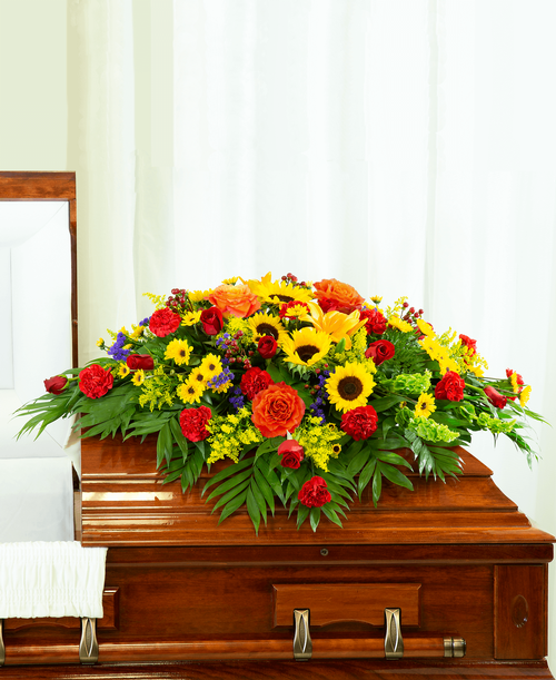 A beautiful half casket spray from our Tuscan Funeral Collection with roses, sunflowers, lilies, bells of Ireland, viking poms, carnations, hypericum, statice, and solidago. 51 inchL x 43 inchW