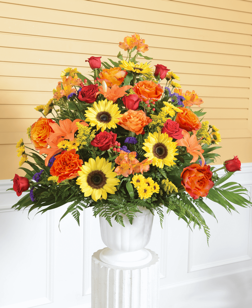 A one-sided arrangement from our Tuscan Funeral Collection, suitable to be sent to a funeral or memorial service, with roses, sunflowers, lilies, viking poms, alstroemeria, hypericum, statice and solidago designed in a 9.5 inch urn. 32 inchH x 32 inchW