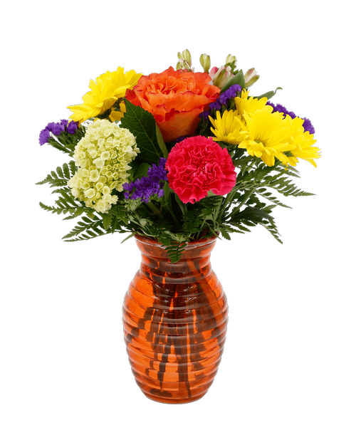 A 7.25 inchH orange glass vase with a horizontal design holds an all around arrangement with an orange rose, a mini green hydrangea, hot pink carnations, pink charmelia alstroemeria, yellow daisy poms, and purple statice. 14 inchH x 10 inchW