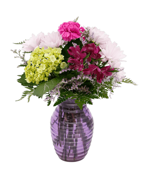 A 7.25 inchH lavender glass vase with a horizontal design holds an all around arrangement with a mini green hydrangea, carnations, alstroemeria, daisy poms, and caspia. 14 inchH x 10 inchW