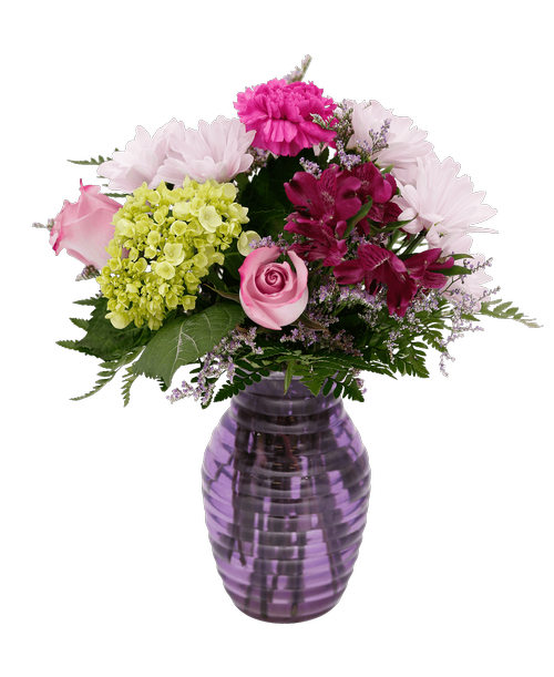 A 7.25 inchH lavender glass vase with a horizontal design holds an all around arrangement with three roses, a mini green hydrangea, carnations, alstroemeria, daisy poms, and caspia. 14 inchH x 10 inchW