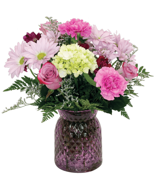A 6.5 inchH lavender glass vase with a diamond pattern holds an all-around arrangement with three roses, a mini green hydrangea, alstroemeria, carnations, mini carnations, daisy poms, and caspia. 14.5 inchH x 11 inchW