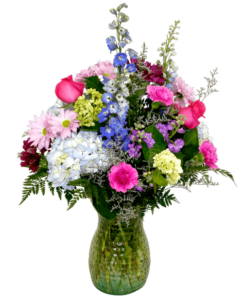 A 10 inch pebbled glass vase holds an all-around arrangement with three roses, hydrangea, delphinium, stock, alstroemeria, mini green hydrangea, daisy poms, carnations, and caspia. 28 inchH x 18 inchW