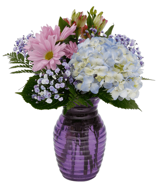 A 7.25 inchH purple glass vase with a horizontal design holds an all around arrangement with a blue hydrangea, lavender daisy poms, charmelia alstroemeria, and purple dyed baby's breath. 13 inchH x 10 inchW
