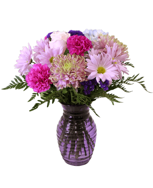 A 7.25 inchH purple glass vase with a horizontal design holds an all around arrangement with a blue hydrangea, a pink rose, football mums, lavender carnations, lavender daisy poms, and purple statice. 15 inchH x 12 inchW
