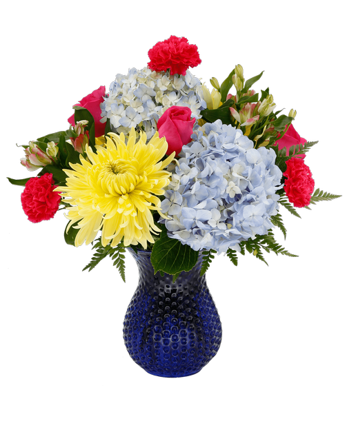 A 7.5 inch cobalt blue dimpled glass vase holds an all around arrangement with three pink roses, blue hydrangea, hot pink carnations, yellow football mums, and pink charmelia alstroemeria. 18 inchH x 15 inchW