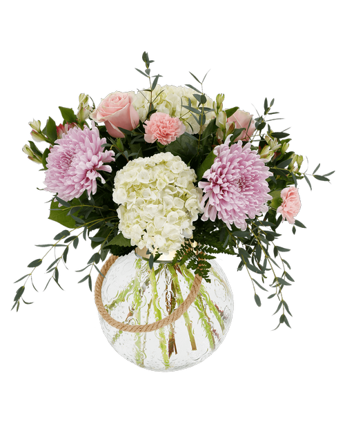 A 10 inchH round clear glass vase with a gold metal rim and a rope handle holds an all around arrangement with three pink roses, white hydrangea, lavender football mums, pink charmelia alstroemeria, pink carnations, and assorted greens. 18 inchH x 18 inchW