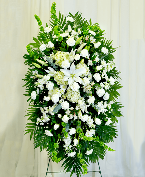 A standing spray from our Celestial Funeral Collection with roses, hydrangea, stock, lilies, carnations, cushion poms, alstroemeria, bells of Ireland, and assorted greens. 57 inchL x 33 inchW