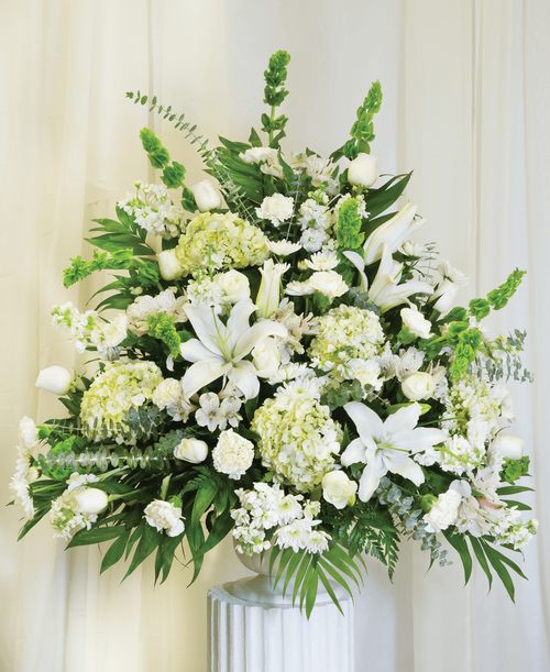 A one-sided arrangement from our Celestial Funeral Collection, suitable to be sent to a funeral or memorial service, with roses, hydrangea, stock, lilies, carnations, cushion poms, alstroemeria, bells of Ireland, and assorted greens designed in a 9.5 inch pedestal urn. 38 inchH x 36 inchW