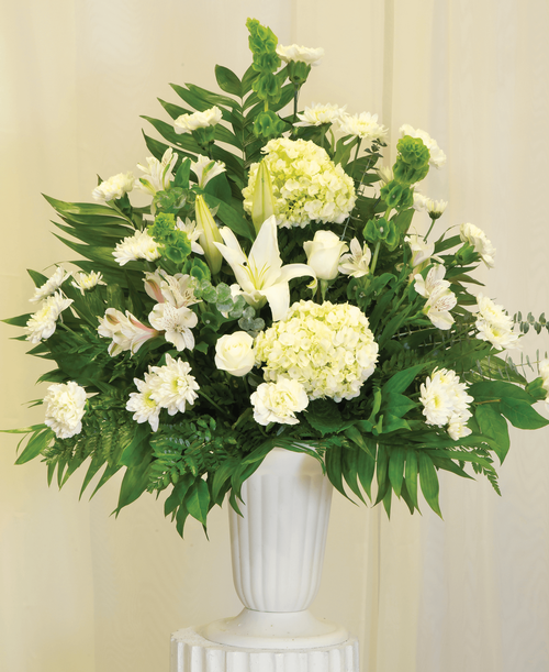 A one-sided arrangement from our Celestial Funeral Collection, suitable to be sent to a funeral or memorial service, with roses, hydrangea, lilies, carnations, cushion poms, alstroemeria, bells of Ireland, and assorted greens designed in a 11-1/4 inch urn. 34 inchH x 27 inchW