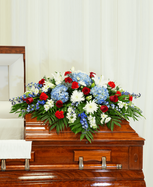 A half casket spray from our Patriotic Funeral Collection with roses, hydrangea, lilies, delphinium, stock, carnations, football mums, cushion poms, eryngium, and assorted greens. 52 inchL x 46 inchW
