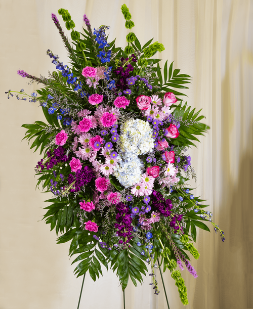 A standing spray from our Tranquil Funeral Collection, suitable to be sent to a funeral or memorial service, with roses, hydrangea, delphinium, stock, liatris, bells of Ireland, carnations, daisy poms, statice, caspia, and assorted greens. 51 inchL x 30 inchW - Displayed on a 54 inch Easel