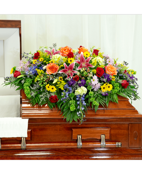 A half casket spray from our English Garden Funeral Collection, with roses, hydrangea, delphinium, stock, lilies, alstroemeria, bells of Ireland, daisy poms, viking poms, solidago, caspia, and assorted greens. 54 inchL x 42 inchW