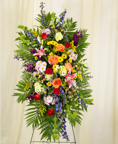 A standing spray from our English Garden Funeral Collection, suitable to be sent to a funeral or memorial service, with roses, hydrangea, delphinium, stock, lilies, alstroemeria, bells of Ireland, daisy poms, viking poms, solidago, caspia, and assorted greens. 60 inchH x 32 inchW - Displayed on a 60 inch Easel