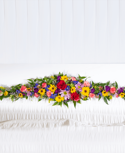 A ledgepiece from our English Garden Funeral Collection to be placed inside the casket and suitable to be displayed at a funeral or memorial service, is designed with roses, delphinium, stock, daisy poms, viking poms, alstroemeria, mini carnations, caspia, solidago. 33 inchL x 6 inchW