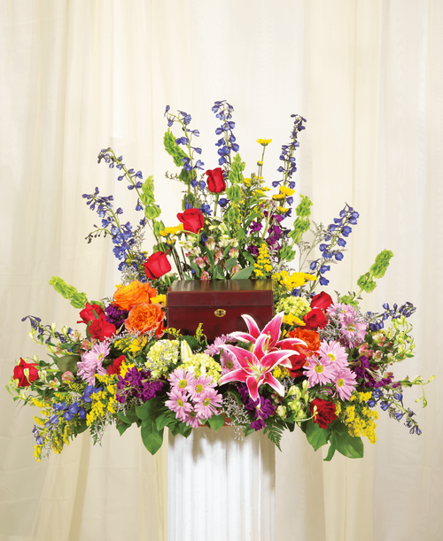 A one-sided arrangement from our English Garden Funeral Collection, with roses, hydrangea, bells of Ireland, lilies, stock, delphinium, alstroemeria, daisy poms, viking poms, solidago, caspia, and assorted greens. Suitable for a funeral or memorial service with the option to display an urn, photo, or a special memento. 31 inchH x 36 inchW