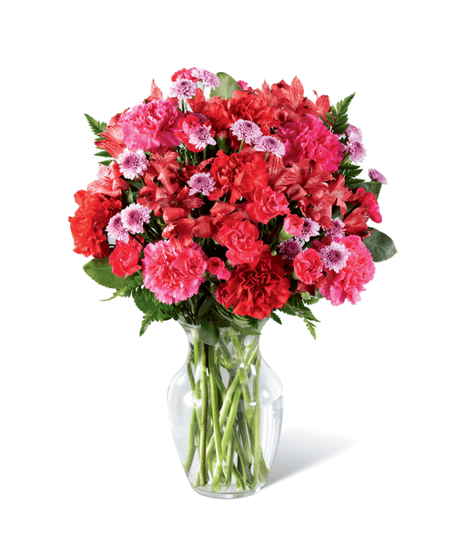 Brilliantly rosy in color, this fresh flower arrangement is out to have your recipient tickled pink with delight. Hot pink carnations and mini carnations start as the color base surrounded by the deeper red hues of roses, carnations, and Peruvian Lilies, accented with the lighter shade brought on by lavender button poms contrasting with assorted greens for a full and lush effect. Presented in a classic clear glass vase, this eye-catching flower bouquet is a standout thank you, thinking of you, or happy birthday gift. Approx. 15 inchH x 12 inchW.