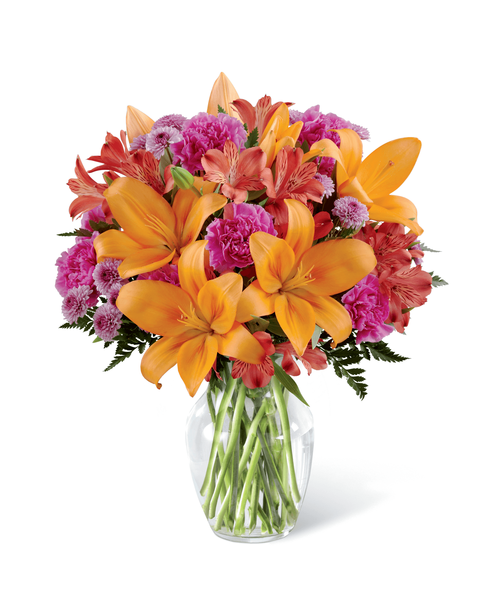 They always brighten your day and now it's time to return the favor. Send light and love with this gorgeous flower arrangement, bringing together orange Asiatic Lilies, fuchsia carnations, and red Peruvian Lilies, beautifully accented with lavender button poms and lush greens in a classic clear glass vase. A warm and sunny way to express your appreciation for your recipient's place in your life, this flower bouquet is that perfect birthday, anniversary, or thank you gift! Approx. 16 inchH x 14 inchW.