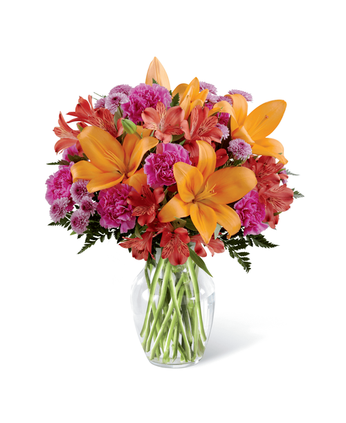 They always brighten your day and now it's time to return the favor. Send light and love with this gorgeous flower arrangement, bringing together orange Asiatic Lilies, fuchsia carnations, and red Peruvian Lilies, beautifully accented with lavender button poms and lush greens in a classic clear glass vase. A warm and sunny way to express your appreciation for your recipient's place in your life, this flower bouquet is that perfect birthday, anniversary, or thank you gift! Approx. 12 inchH x 10 inchW.