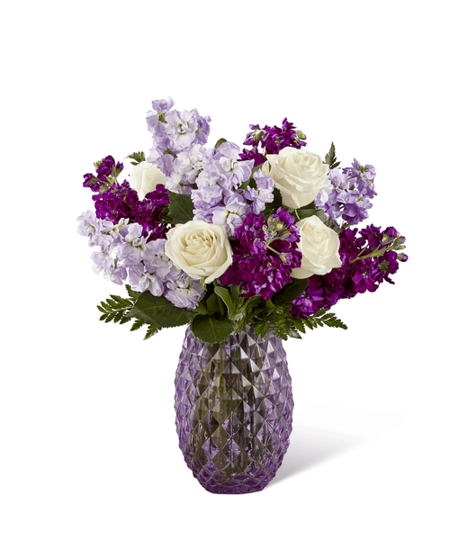 FTD proudly presents the Better Homes & Gardens Sweet Devotion Bouquet. Purple is a shade that captivates the imagination and inspires, with it's fascinating cool shades of light and dark. Bringing together a collection of purple's finest blooms, this enchanting bouquet offers a combination of the swirling petals of lavender roses, the fragrant stalks of purple and lavender gilly flower, and purple statice accented with clusters of green button poms and lush greens. Arranged to perfection within an attractive keepsake purple glass vase, this gorgeous flower bouquet is ready to create a special birthday, anniversary, or thinking of you moment! Approx. 19 inchH x 15 inchW