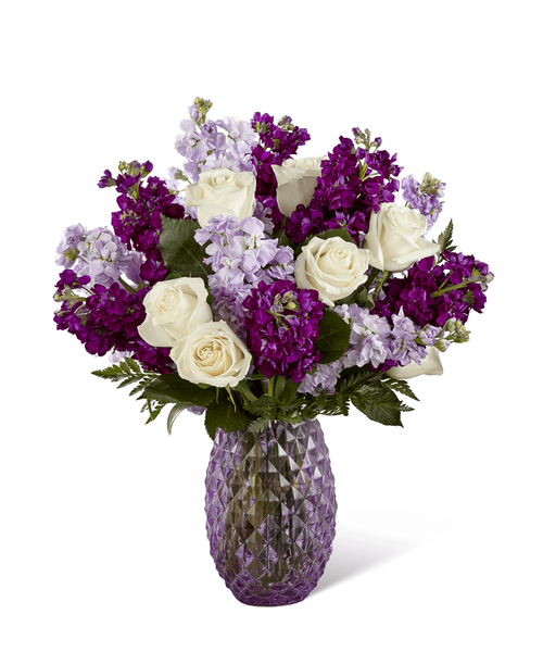 FTD proudly presents the Better Homes & Gardens Sweet Devotion Bouquet. Purple is a shade that captivates the imagination and inspires, with it's fascinating cool shades of light and dark. Bringing together a collection of purple's finest blooms, this enchanting bouquet offers a combination of the swirling petals of lavender roses, the fragrant stalks of purple and lavender gilly flower, and purple statice accented with clusters of green button poms and lush greens. Arranged to perfection within an attractive keepsake purple glass vase, this gorgeous flower bouquet is ready to create a special birthday, anniversary, or thinking of you moment! Approx. 20 inchH x 18 inchW