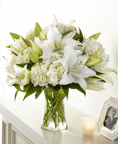 Classic lily and hydrangea blooms are designed by a local florist t create our Compassionate Lily Bouquet. Each white bloom elegantly brings solace and comfort t those experiencing a loss. Please note that lilies initially come in bud form, only t beautifully transform as they open up. 
Good bouquet is approximately 16 inchH x 16 inchW 
Better bouquet is approximately 18 inchH x 17 inchW 
Best bouquet is approximately 19 inchH x 20 inchW 