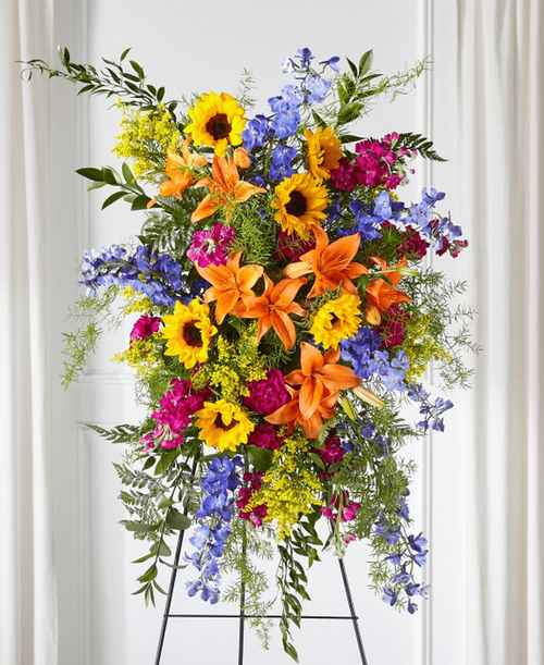 Sunlit Memories Standing Spray is crafted with a mix of fuchsia, deep blue, hot pink and orange florals to celebrate their radiant life. 36 inchHx25 inchW